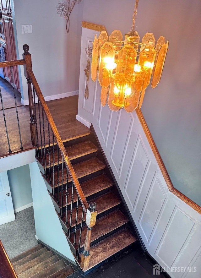 stairway featuring baseboards, wood finished floors, and a notable chandelier