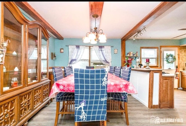 dining room with light wood-style floors, beam ceiling, and an inviting chandelier