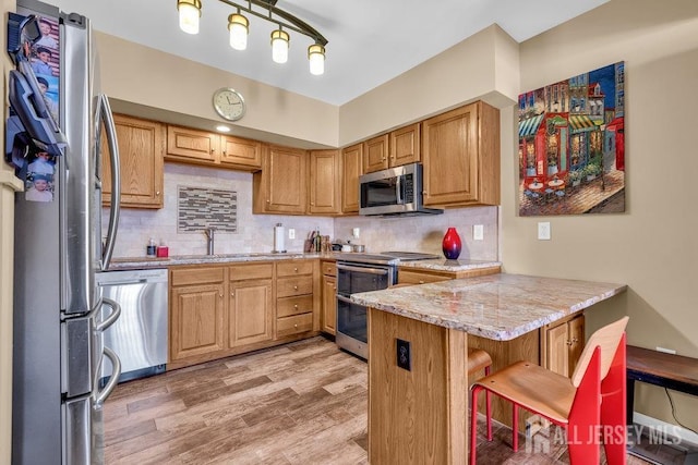 kitchen featuring a kitchen breakfast bar, kitchen peninsula, stainless steel appliances, light stone countertops, and light hardwood / wood-style floors