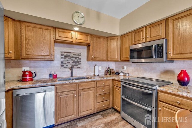 kitchen with sink, appliances with stainless steel finishes, tasteful backsplash, light hardwood / wood-style floors, and light stone countertops