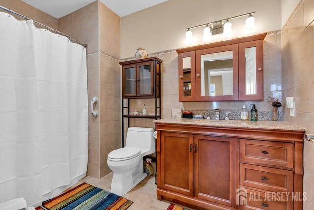 bathroom with tile patterned floors, toilet, tile walls, vanity, and backsplash