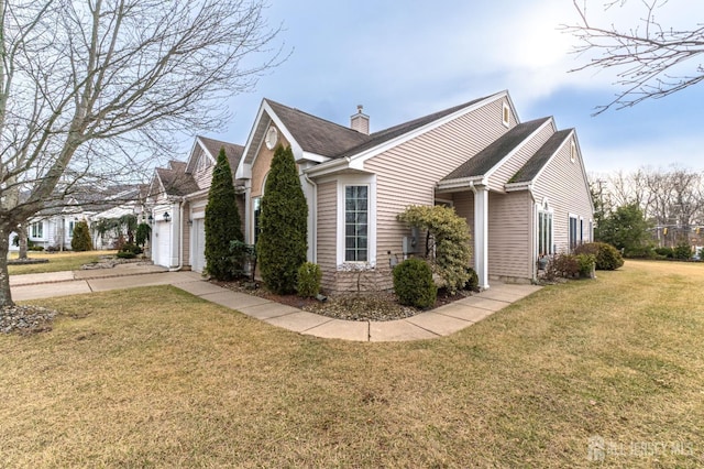 view of side of home featuring an attached garage, driveway, a lawn, and a chimney