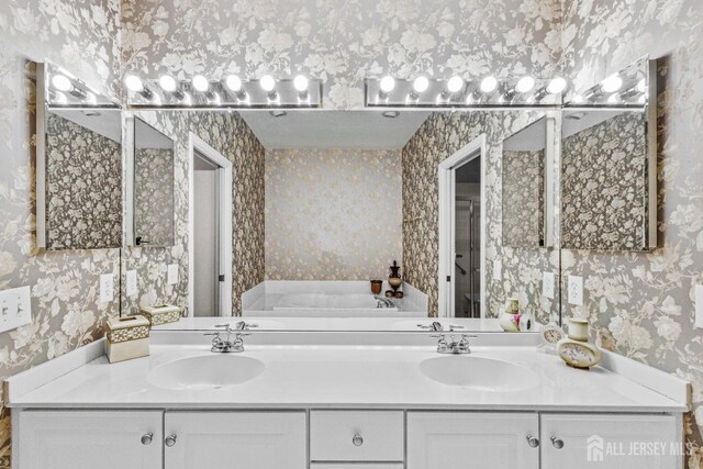 full bath with double vanity, a sink, and wallpapered walls