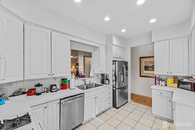 kitchen with light countertops, backsplash, appliances with stainless steel finishes, white cabinetry, and a sink