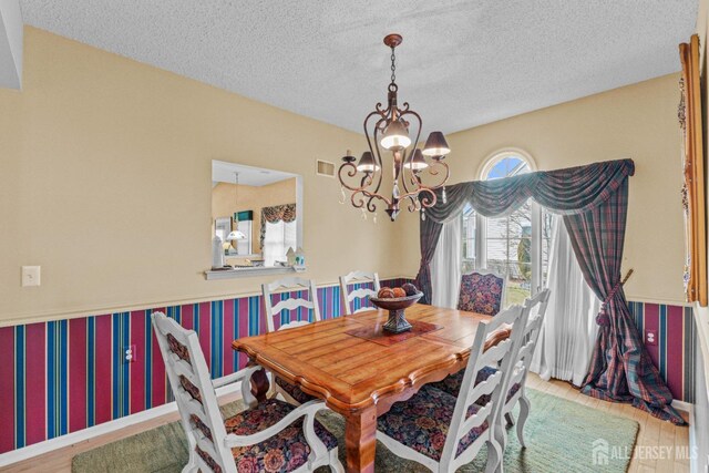 dining space featuring a chandelier, a textured ceiling, wood finished floors, visible vents, and wallpapered walls