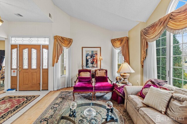 entrance foyer featuring a wealth of natural light, visible vents, vaulted ceiling, and wood finished floors