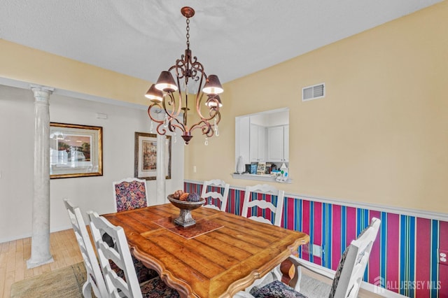 dining space featuring visible vents, decorative columns, a notable chandelier, and wood finished floors