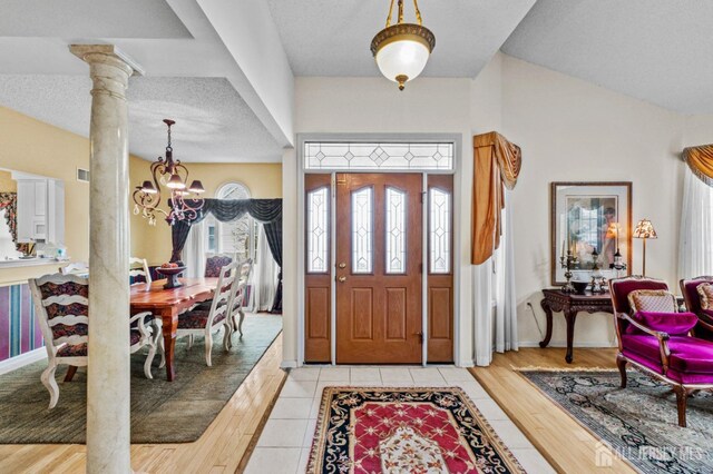 entrance foyer featuring visible vents, an inviting chandelier, a textured ceiling, light wood-type flooring, and ornate columns