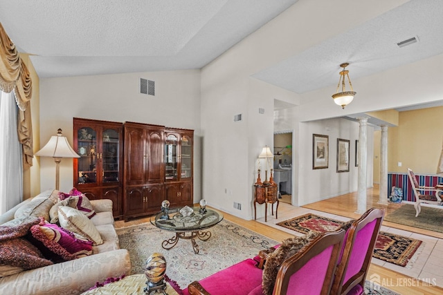 living area featuring lofted ceiling, ornate columns, visible vents, and a textured ceiling