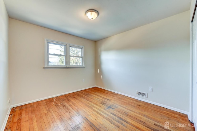 spare room featuring light wood-type flooring, visible vents, and baseboards