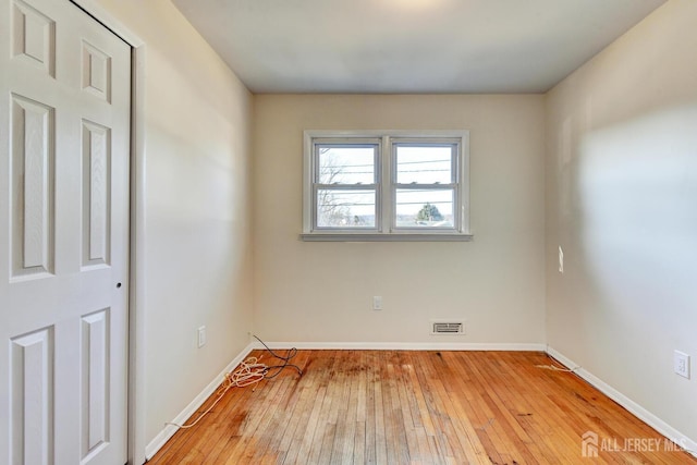 spare room with wood-type flooring, visible vents, and baseboards