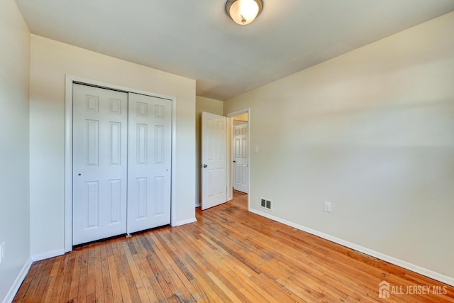 unfurnished bedroom featuring light wood-style flooring, a closet, visible vents, and baseboards