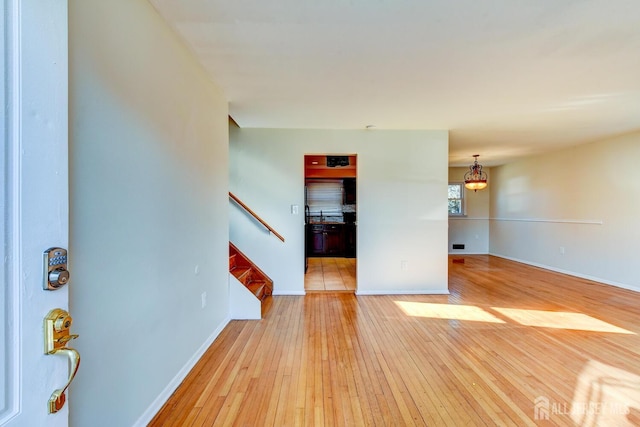 unfurnished living room featuring light wood finished floors, baseboards, and stairway