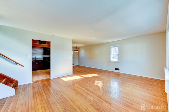 unfurnished living room featuring baseboards, visible vents, light wood finished floors, and stairs