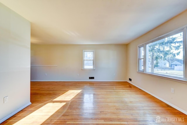 unfurnished room with baseboards, visible vents, plenty of natural light, and light wood finished floors