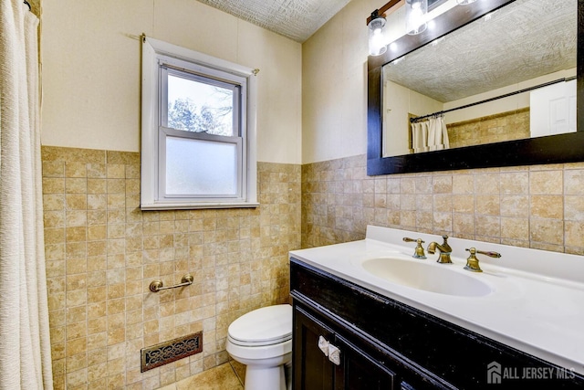 bathroom featuring wainscoting, toilet, a textured ceiling, vanity, and tile walls