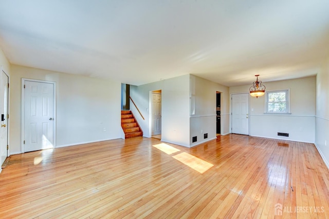 unfurnished living room with light wood-type flooring, baseboards, stairs, and visible vents