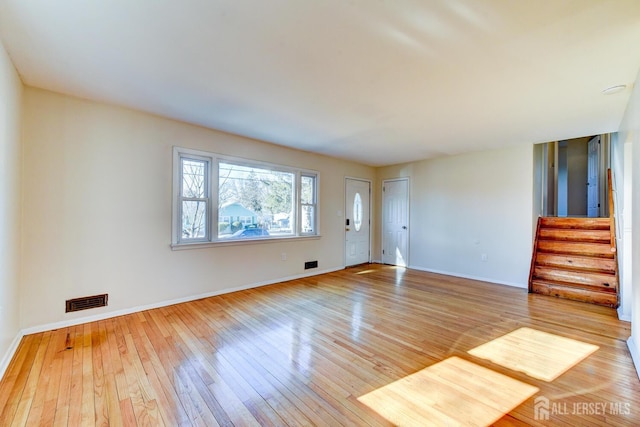 unfurnished living room with baseboards, stairs, visible vents, and hardwood / wood-style floors