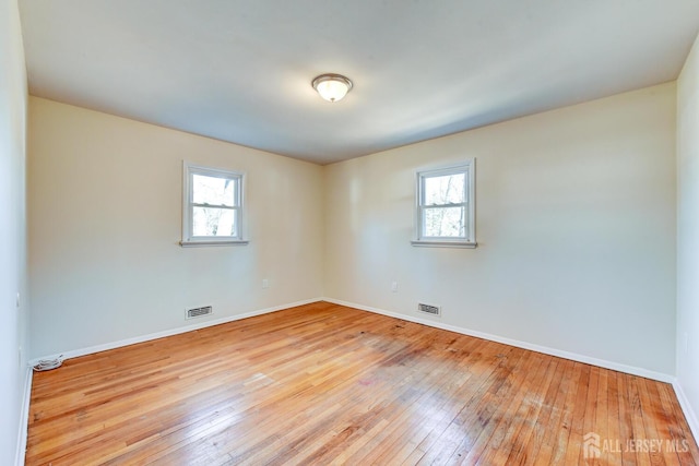 empty room featuring a wealth of natural light, visible vents, and hardwood / wood-style floors