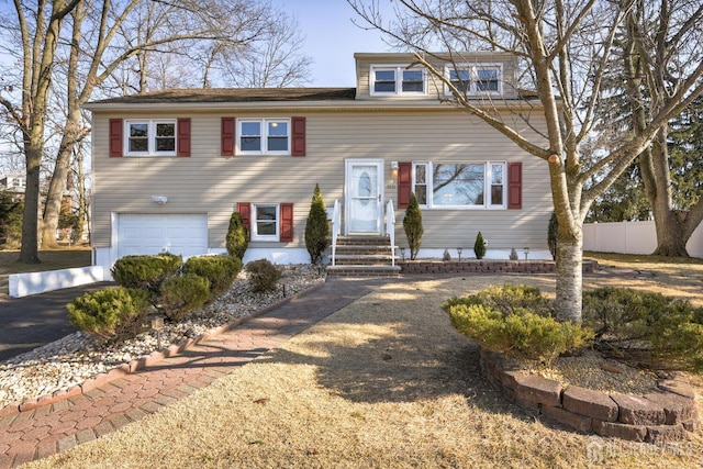 view of front of house with entry steps, fence, driveway, and an attached garage