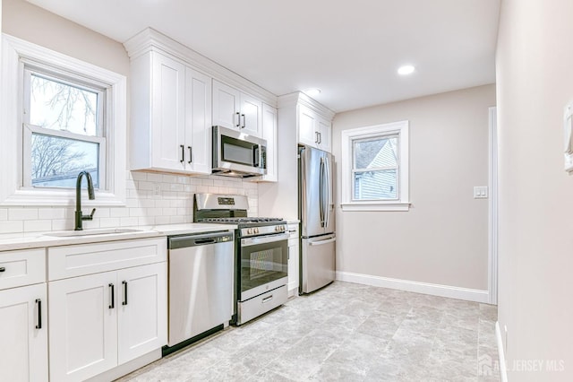 kitchen featuring baseboards, decorative backsplash, white cabinets, appliances with stainless steel finishes, and a sink