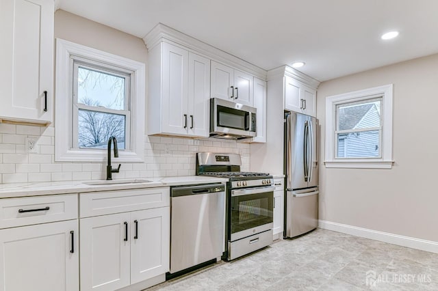 kitchen with light stone counters, decorative backsplash, appliances with stainless steel finishes, white cabinetry, and a sink