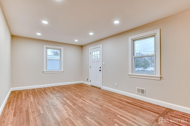 empty room with light wood-style floors, a wealth of natural light, visible vents, and baseboards