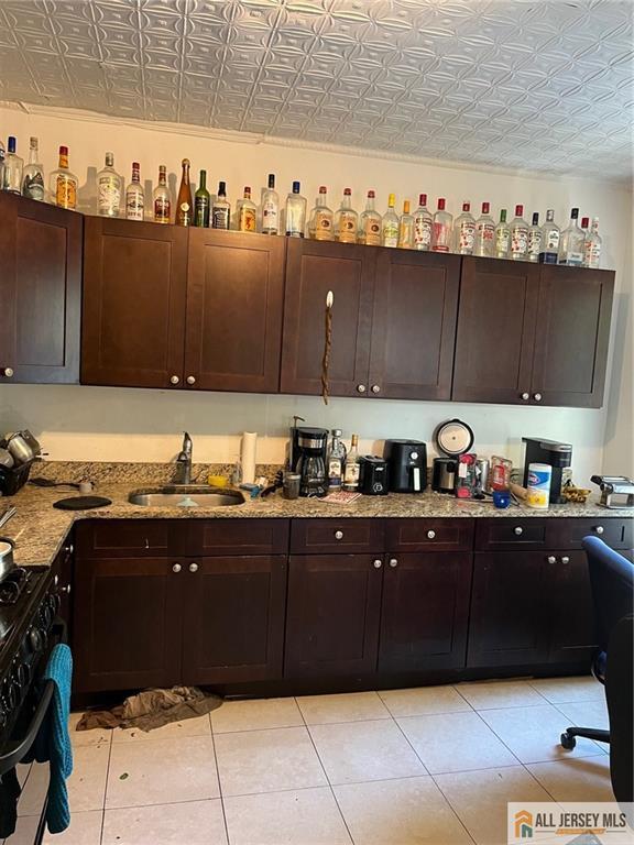 kitchen with light tile patterned floors, dark brown cabinets, sink, and black range with gas cooktop