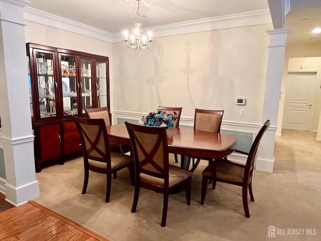 dining room featuring decorative columns, ornamental molding, a notable chandelier, and light carpet