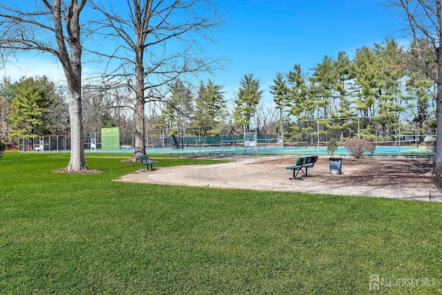 view of community with a tennis court, a yard, and fence