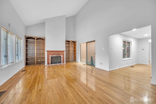 unfurnished living room featuring light wood-type flooring, high vaulted ceiling, visible vents, and a fireplace