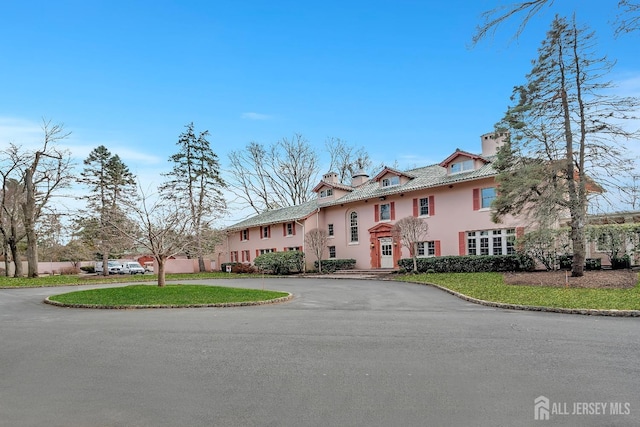 view of front facade featuring aphalt driveway, a chimney, a front lawn, and stucco siding