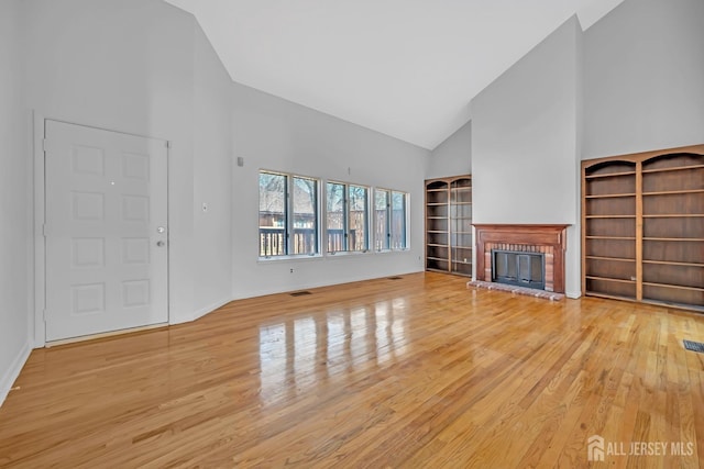 unfurnished living room with visible vents, a fireplace, high vaulted ceiling, and wood finished floors