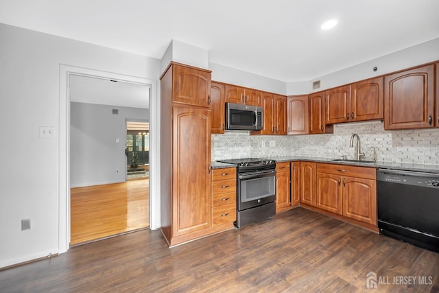 kitchen featuring dark wood-type flooring, decorative backsplash, brown cabinetry, black appliances, and a sink