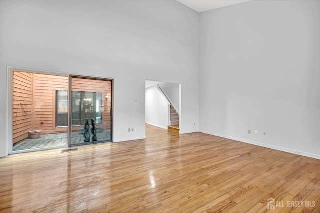 unfurnished living room featuring stairway, wood finished floors, visible vents, and baseboards