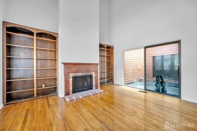 unfurnished living room with visible vents, a fireplace, a high ceiling, and wood finished floors