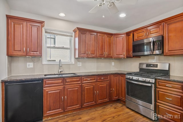 kitchen with stainless steel appliances, dark wood-type flooring, a sink, a ceiling fan, and dark stone counters