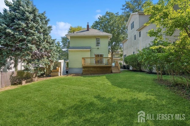 rear view of house featuring a lawn, a chimney, a wooden deck, and fence