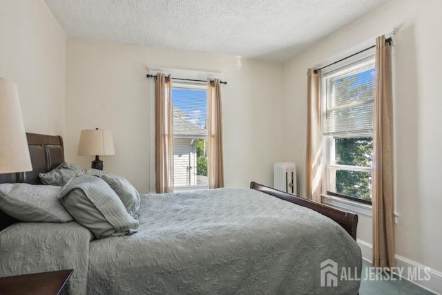 bedroom with a textured ceiling, multiple windows, radiator heating unit, and baseboards