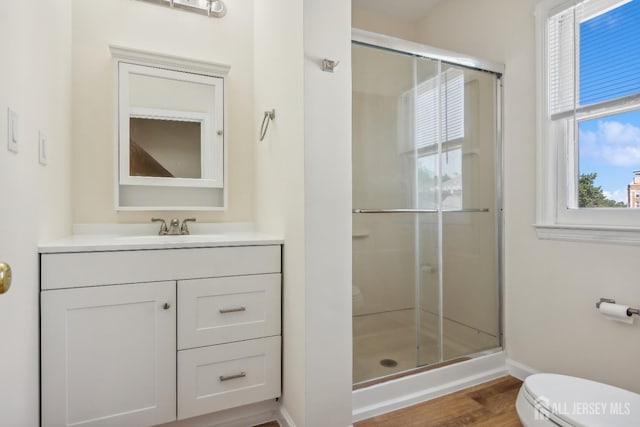 bathroom with toilet, wood finished floors, vanity, baseboards, and a stall shower