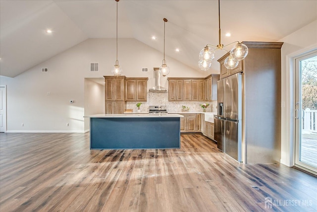 kitchen featuring appliances with stainless steel finishes, backsplash, hanging light fixtures, a center island, and wall chimney exhaust hood