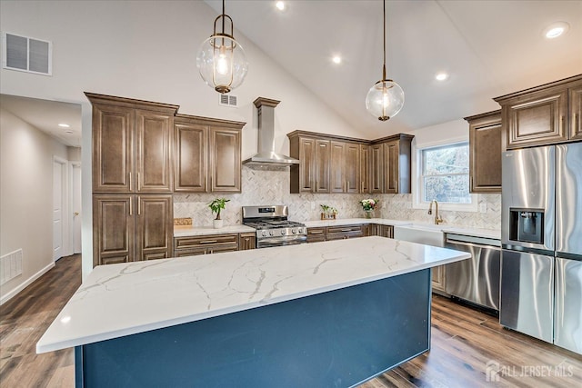 kitchen with pendant lighting, appliances with stainless steel finishes, a kitchen island, and wall chimney range hood