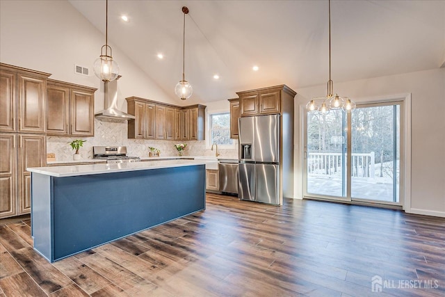 kitchen with wall chimney exhaust hood, tasteful backsplash, a center island, appliances with stainless steel finishes, and pendant lighting