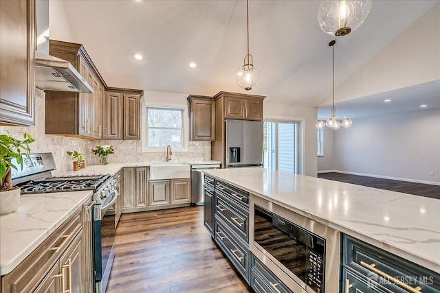 kitchen with sink, stainless steel appliances, light stone counters, vaulted ceiling, and wall chimney exhaust hood