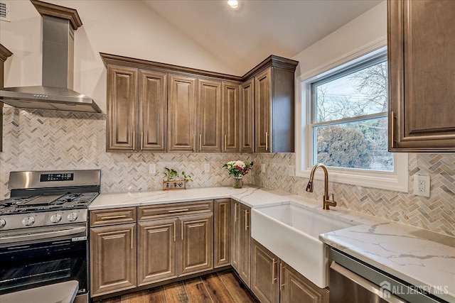 kitchen featuring wall chimney exhaust hood, sink, vaulted ceiling, appliances with stainless steel finishes, and dark hardwood / wood-style floors