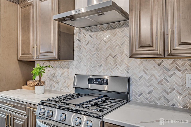 kitchen with light stone counters, gas range, and wall chimney exhaust hood