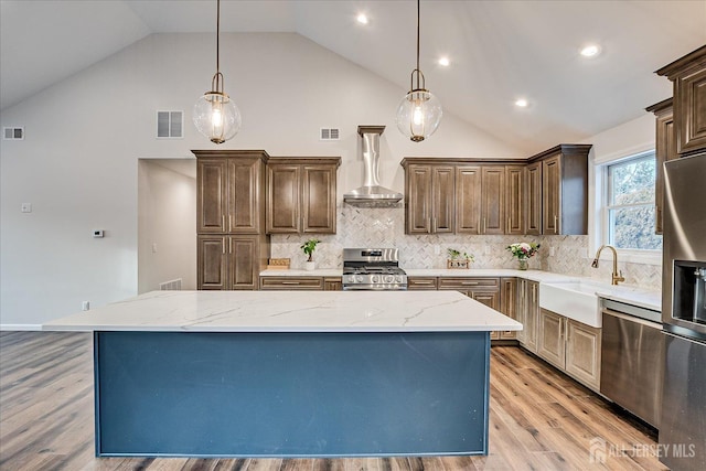 kitchen featuring wall chimney exhaust hood, stainless steel appliances, decorative light fixtures, and a kitchen island