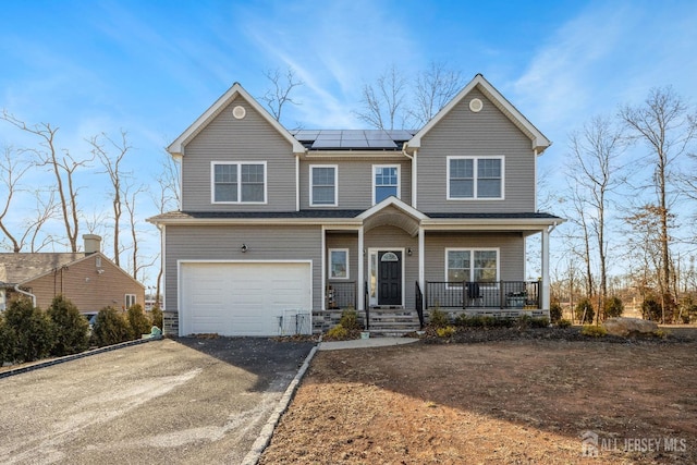 view of front of house with a porch, asphalt driveway, roof mounted solar panels, and an attached garage