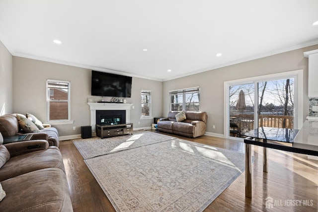 living room featuring ornamental molding, wood finished floors, baseboards, recessed lighting, and a glass covered fireplace