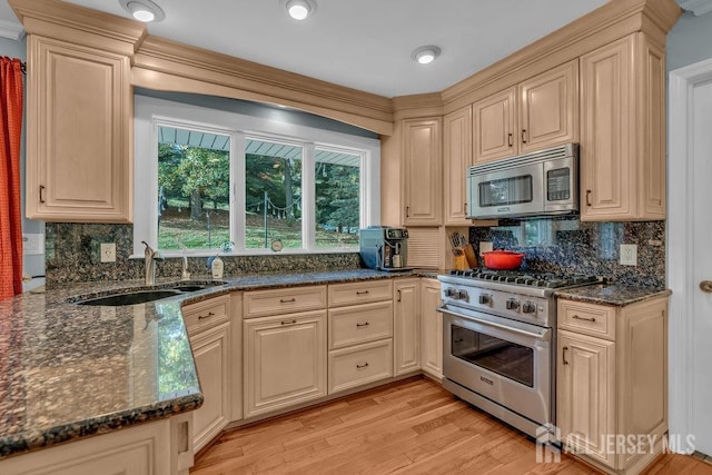 kitchen featuring appliances with stainless steel finishes, sink, light wood-type flooring, backsplash, and dark stone countertops